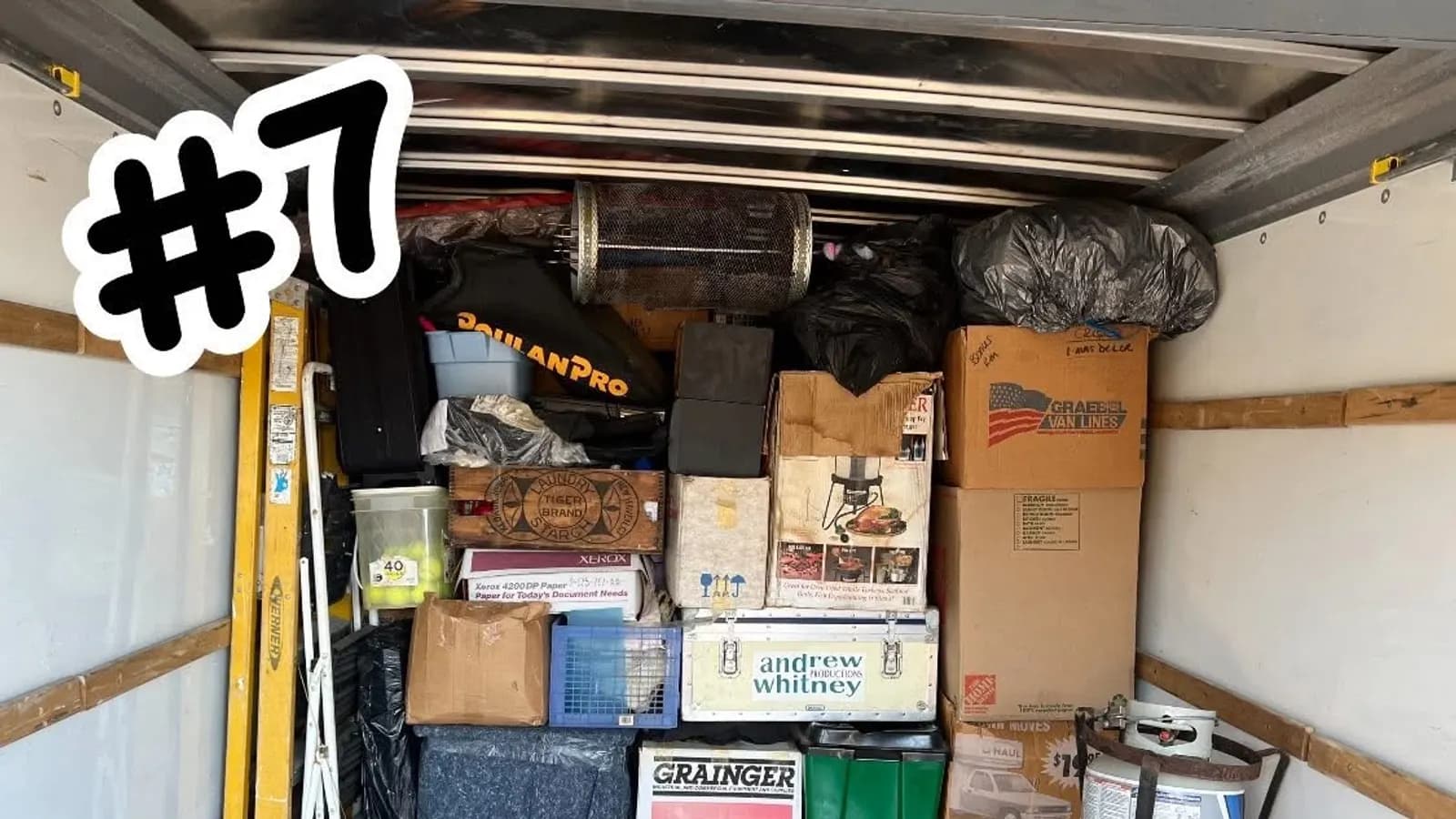 Moving truck loaded with boxes, a ladder, equipment trunks, and garage gear secured for transport